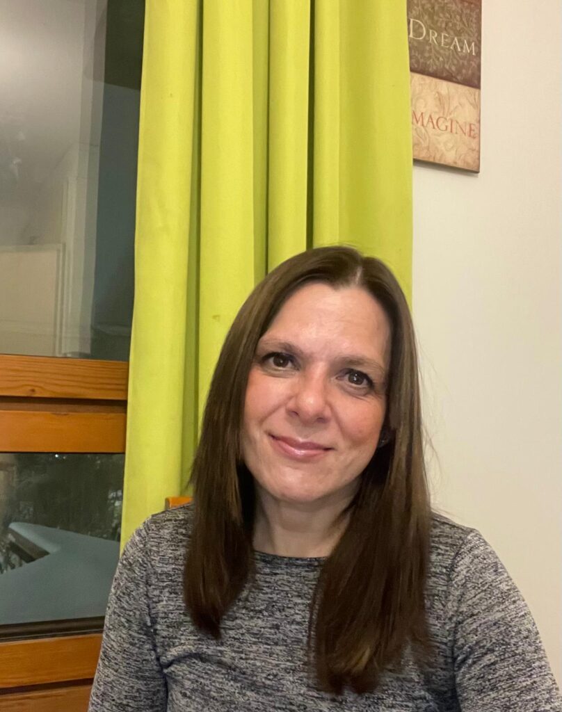 Hymyilevä hyvinvointialan ammattilainen sisätiloissa, taustalla vaaleanvihreät verhot.